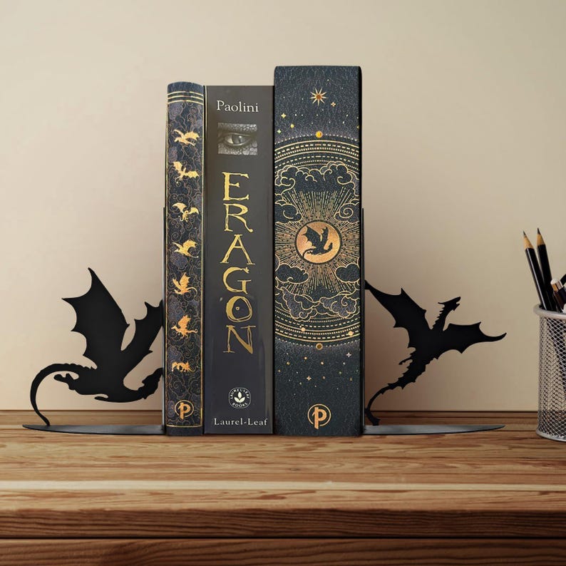 May include: Black metal dragon bookends holding three books. The books are dark with gold lettering and accents. The bookends are on a wooden surface with a pencil holder in the background.