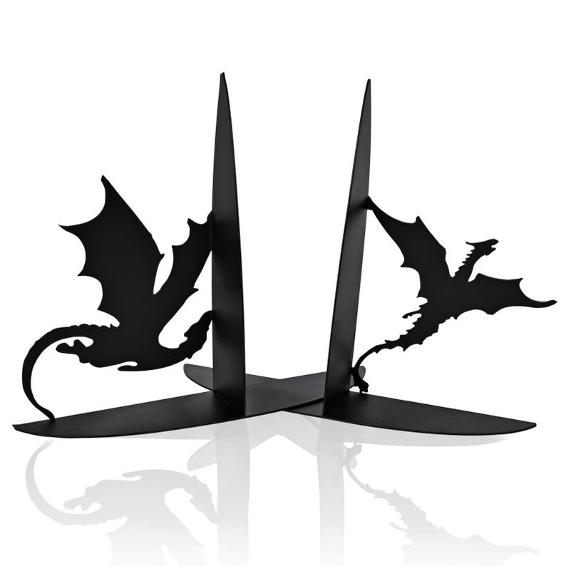 May include: Black metal bookends featuring dragon silhouettes. The bookends have a minimalist design with two vertical supports and a base that intersects to form an X shape. The dragons are depicted in flight, adding a fantasy element to the functional decor.