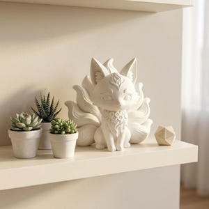 Peut inclure: Une figurine blanche mate représentant un renard à neuf queues avec des motifs sculptés complexes sur la poitrine et le front. Le renard est assis avec ses multiples queues déployées derrière lui, à côté de trois petites plantes succulentes.