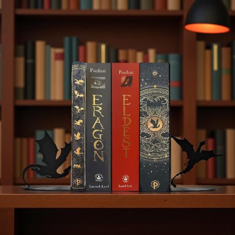 May include: Four hardcover books with the titles "Eragon" and "Eldest" are displayed between two black metal dragon-shaped bookends. The books are on a wooden shelf in front of a bookshelf.