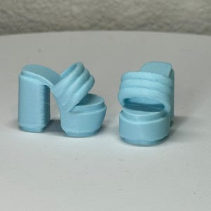 May include: A pair of light blue platform sandals. Each sandal has a thick, rounded heel and a platform sole. The straps across the top of the foot are padded. The heels are approximately 3 inches tall.