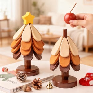 May include: Two wooden Christmas tree decorations with a star and a red apple. The trees are made of layered wooden pieces in shades of brown, orange, and beige. A small red and white stocking, pine cones, and a bell are also on the table.