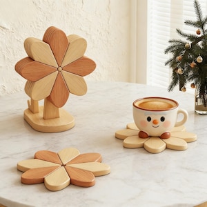 May include: A wooden flower-shaped coaster set with a matching stand. The coasters and stand are made of light and medium-toned wood. A ceramic mug with a smiling face sits on one of the coasters. A small Christmas tree is in the background.
