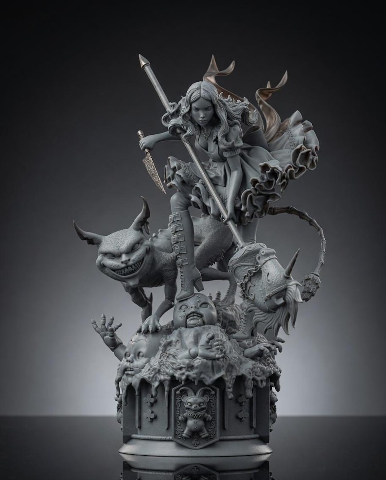 May include: A gray resin statue featuring a figure in a ruffled dress holding a long spear and a dagger, standing atop a creature with a wide grin. The base includes a sculpted doll head and a central emblem of a jester-like figure with pointed ears.