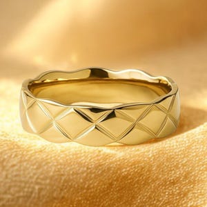 Op de afbeelding: Een goudkleurige ring met een gewatteerd patroon. De ring heeft een golvende rand en een glanzende afwerking. De ring is een bandstijl en het ontwerp is een reeks ruitvormen. De ring is waarschijnlijk van metaal.