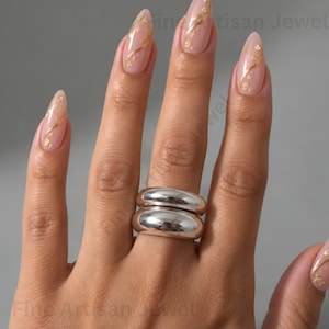 May include: Two stacked silver-toned rings with a smooth, polished, and rounded surface. The rings feature a thick, domed band design that sits flush against each other, creating a continuous, reflective metallic appearance on the finger.