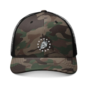 May include: A camouflage trucker cap featuring a black mesh back and a front panel with a green, brown, and black camo pattern. Centered on the front is an embroidered white graphic of a skull wearing a crown, surrounded by a circle of stars.