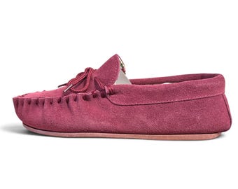 May include: A deep magenta suede moccasin shoe featuring a rounded toe, a decorative lace-up tie detail on the top, and a whipstitched seam along the front edge. The shoe has a flat sole and a visible floral patterned lining inside the collar.