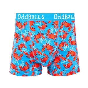 May include: Boxer briefs in a bright blue colour featuring a repeating pattern of orange-red crabs. The waistband is a matching blue with the white text OddBalls printed repeatedly across the front. The garment has visible stitching details.