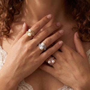 May include: Three rings featuring two white pearls each, set on multi-band shanks encrusted with small clear stones. One ring is gold-toned, one is silver-toned, and one is rose gold-toned, each worn on a different finger to showcase the design.