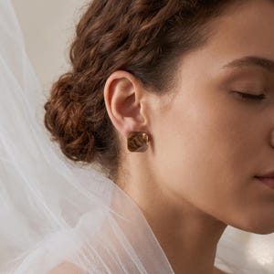 Peut inclure: Une boucle d'oreille à clou de forme carrée en résine translucide brun chaud, présentant un motif tourbillonnant subtil. La boucle d'oreille possède une surface lisse et polie ainsi qu'un design géométrique qui repose contre le lobe.