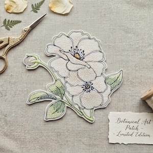Könnte beinhalten: Gestickter Blumenaufnäher mit zwei weißen Blüten mit gelben Zentren und grünen Blättern. Der Aufnäher trägt die Aufschrift "Botanical Art Patch - Limited Edition."