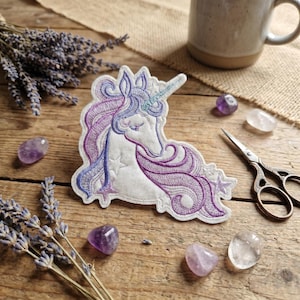 Puede incluir: Parche de unicornio bordado con cuerpo blanco, melena morada y cuerno azul. El parche está rodeado de ramitas de lavanda, cristales de amatista y una taza. El parche mide aproximadamente 10 cm de ancho y 7,5 cm de alto.