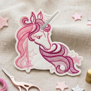 Könnte beinhalten: Gestickter Einhorn-Aufnäher in Weiß und Rosatönen, mit silbernem Horn und Sternakzenten. Der Aufnäher hat detaillierte Nähte und ein skurriles Design, ideal für Kleidung oder Accessoires.
