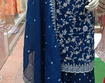 May include: A deep blue three-piece outfit consisting of a long-sleeved tunic, wide-leg pants, and a matching dupatta. The tunic features intricate silver and light pink floral embroidery, a round neckline, and a scalloped hem with detailed trim.