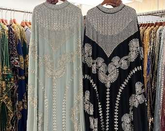 May include: Two floor-length kaftans, one in pale mint green and one in black, both featuring high necklines and extensive silver beadwork, sequins, and crystal embellishments arranged in intricate geometric and floral patterns.