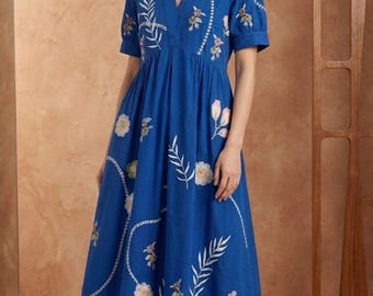 May include: A vibrant blue midi dress featuring a V-neckline, short puff sleeves, and an empire waist. The fabric is adorned with white and muted-tone embroidered floral and botanical patterns, including delicate leaf sprigs and circular blooms.