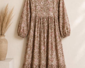 May include: A long-sleeved midi dress in a muted taupe color featuring an all-over floral print in shades of white, pink, and dark green. The dress has a round neckline, a gathered waistline, and a tiered skirt with a ruffled hemline.