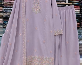 May include: A light purple three-piece outfit consisting of a long-sleeved tunic, wide-leg trousers, and a matching dupatta. The tunic features intricate floral embroidery around the neckline, cuffs, and hem, with scattered floral motifs throughout.