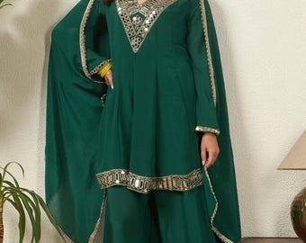 May include: A dark green tunic and wide-leg pants set featuring a V-neckline adorned with silver-toned mirror work embroidery. The tunic includes long, flowing cape-style sleeves with gold-toned trim, and the hem is detailed with matching mirror work.
