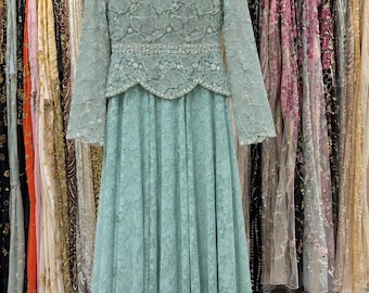 May include: A floor-length, long-sleeved dress in a soft sage green hue, featuring intricate floral lace embroidery throughout. The bodice includes a scalloped waistline and a high neckline, both embellished with delicate beads and sequins.