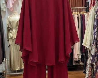 May include: A deep burgundy two-piece outfit consisting of a long-sleeved tunic and wide-leg trousers. The tunic features a high neckline adorned with fabric roses and hanging beaded fringe accents, crafted from a flowing, semi-sheer fabric.
