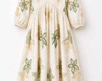 May include: A cream-colored midi dress featuring a V-neckline, three-quarter length sleeves, and a ruffled hem. The fabric is adorned with embroidered floral patterns in shades of olive green and tan, with green stitching along the neckline.