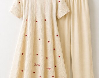 May include: A cream-colored short-sleeved dress and matching wide-leg trousers set. The dress features a textured fabric with small embroidered red hearts and the cursive text "Be you", "magic", and "love" scattered across the front skirt.