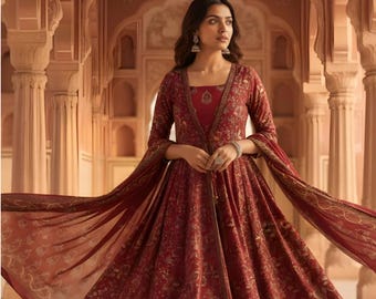 May include: A deep red floor-length dress featuring a complex gold floral pattern, a square neckline, and long sleeves. The garment includes a matching sheer shawl draped over the arms and a coordinating pair of trousers visible at the hemline.
