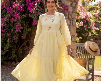 May include: A pale yellow midi dress featuring long sleeves, a tiered skirt, and a sheer yoke neckline. The bodice is decorated with small, embroidered yellow floral motifs. The dress has a loose, flowing silhouette and a gathered waistline.