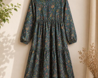 May include: A long-sleeved teal dress featuring a multi-colored floral print, a round neckline, and a tiered skirt. The dress is displayed on a wooden hanger with the brand name FIXELIA printed on the label and the text TEAL JAL PRINT DRESS WITH SPEGHTIE.