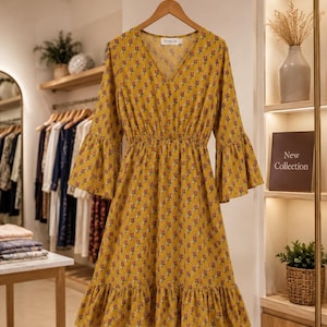 May include: A mustard yellow knee-length dress featuring a repeating pattern of small red and green floral motifs. The garment has a V-neckline, three-quarter length bell sleeves, a cinched waist, and a ruffled hemline with a label reading PIXELIA.