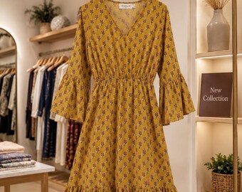 May include: A mustard yellow knee-length dress featuring a repeating pattern of small red and green floral motifs. The garment has a V-neckline, three-quarter length bell sleeves, a cinched waist, and a ruffled hemline with a label reading PIXELIA.
