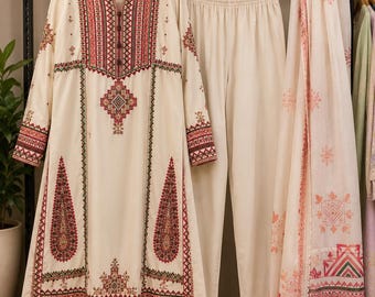 May include: A cream-colored long-sleeved tunic with a split neckline and intricate red and green geometric embroidery, paired with matching cream trousers and a coordinating long scarf featuring a repeating red and green patterned print.