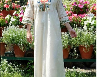May include: A long-sleeved, off-white calf-length tunic dress featuring a V-neckline with colorful floral embroidery in red, yellow, and green. The sleeves have scalloped edges with green vine embroidery, and the garment is paired with matching pants.