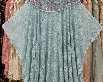 May include: A light blue lace kaftan featuring a high neckline adorned with intricate floral embroidery in shades of pink, blue, and gold. The garment has wide, flowing sleeves and a pleated, floor-length skirt made of delicate, patterned lace fabric.