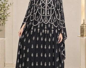 May include: A floor-length black kaftan dress featuring an intricate silver beaded neckline and a cape-style overlay. The garment is adorned with a repeating silver floral embroidery pattern throughout the fabric, creating a cohesive design.