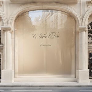 May include: Exterior shot of a storefront with a large arched window. The window displays the name "Aesthe Tori" in elegant script, with "MADE IN ITALY" and a website address below. The building has a classic architectural design with columns and arches.