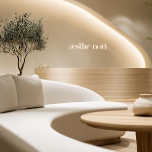 May include: Interior of a spa or salon with a minimalist design. A curved white sofa, wooden coffee table, and a small tree are visible. The wall displays the text "æsthé nori" in a soft, glowing light.
