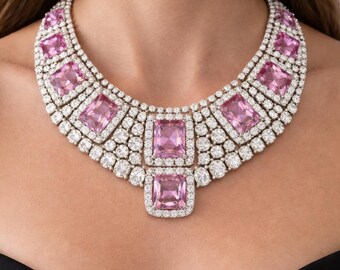 Op de afbeelding: Een statement ketting met meerdere rechthoekige roze edelstenen in een gelaagd patroon. Elke roze steen is omringd door een halo van kleine, heldere, ronde witte steentjes, met extra clusters van heldere steentjes die de segmenten verbinden.