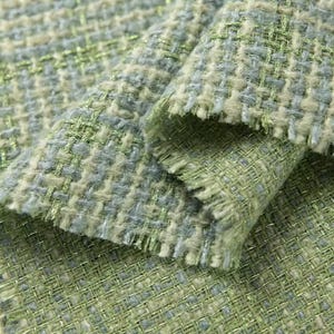 Può includere: Un tessuto intrecciato testurizzato caratterizzato da una miscela di fili verde chiaro, salvia e blu tenue. Il materiale presenta una trama larga e spessa con fibre metalliche dorate visibili, che creano un sottile luccichio sulla superficie.