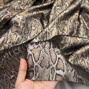 Tessuto morbido e drappeggiato con texture effetto pelle di pitone, tessuto lucido stampato in oro per camicie, abiti e gonne, tessuto di design per accessori.