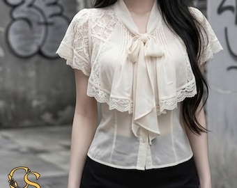 Puede incluir: Una blusa de color crema de manga corta con detalles de encaje en hombros y mangas, cierre frontal de botones y un lazo decorativo en el cuello con volantes. La prenda incluye el logotipo CeleStyleCharm en la esquina inferior.