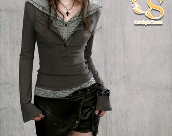 May include: A two-piece outfit featuring a long-sleeved, olive-green hooded top with a button-down front and a layered design. The outfit includes a dark, wrap-style skirt with a belt. The top has a gray hood and a patterned inner layer.