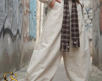 Puede incluir: Pantalones anchos de color blanco roto con diseño de cintura alta y un cinturón largo de tela a cuadros marrones y negros que cuelga de la cintura. Los pantalones tienen bolsillos laterales y un corte holgado, combinados con una blusa a juego.