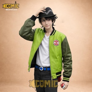Può includere: Una giacca bomber verde e oliva con una camicia bianca sotto. La giacca ha un'emblema rosso e bianco sul petto e polsini a righe nere e gialle. Un cappello nero e una cintura blu completano l'outfit. Una palla rossa e bianca è tenuta in mano.