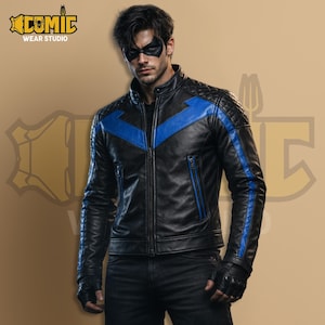 Puede incluir: Chaqueta de cuero negra con detalles azules, incluyendo un diseño de chevron y rayas. La chaqueta tiene un patrón acolchado en los hombros y un cuello alto. El logo de Comic Wear Studio es visible. Con cierre de cremallera.