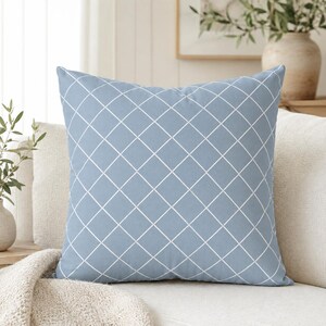 Könnte beinhalten: Ein quadratisches Dekokissen in staubigem Blau mit einem weißen Gittermuster aus dünnen, sich kreuzenden diagonalen Linien, die ein Rautenmuster über die gesamte Vorderseite des Stoffbezugs bilden.