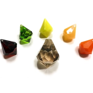 Può includere: Una collezione di oggetti sfaccettati a forma di gemma in vari colori, tra cui rosso, verde, giallo, arancione e marrone. Gli oggetti hanno una forma geometrica, simile a un diamante, e sono disposti su uno sfondo bianco. Sembrano essere decorativi o ornamentali.