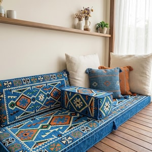 Peut inclure: Un coussin de banc et des coussins bleus avec des motifs géométriques orange, verts et blancs. Le banc est orné de plusieurs coussins décoratifs de différentes couleurs et textures, créant un coin salon confortable.